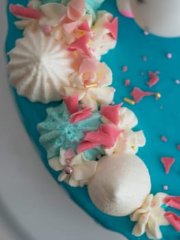 studio shot of chocolate frosted blue dripped icing white cup cake, unicorn , meringue and sprinkles on top