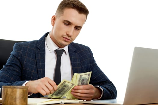 young businessman working on laptop and holding money while sitting on chair at desk.
