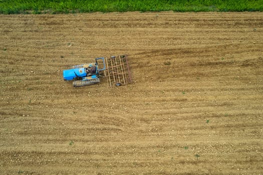 senior farmer driving crawled tractor in plowed dry field before seeding aerial point of view