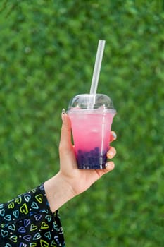 Woman holding bubble tea with lemonade in front of green grass wall