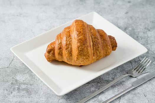 Croissant on white porcelain plate on light stone table