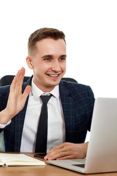 young friendly businessman talking at laptop webcam, sitting on chair at desk, using laptop pc computer
