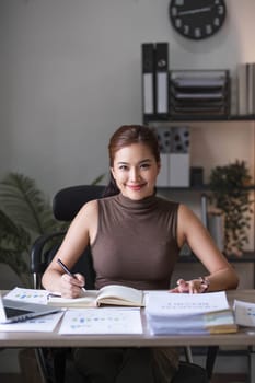 Happy Asian businesswoman working and checking work with laptop computer while having a comfortable cup of coffee at office...