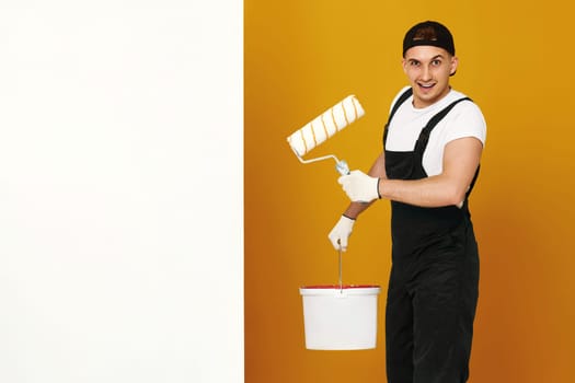 happy man in working clothes winks and paints white walls in the room. copy space for text