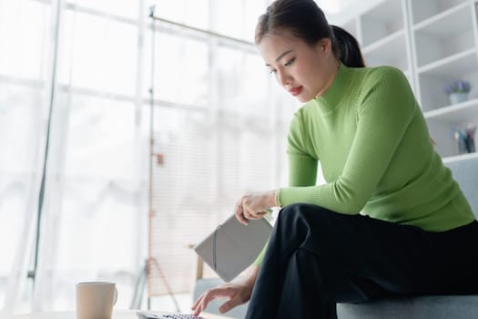 Beautiful asian women working out home finances using calculator to calculating, with invoices and paperwork on desk, living room interior. female economics accounts, cash flow expenses