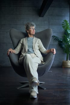 attractive middle aged smiling woman model sitting in chair looking at camera at office