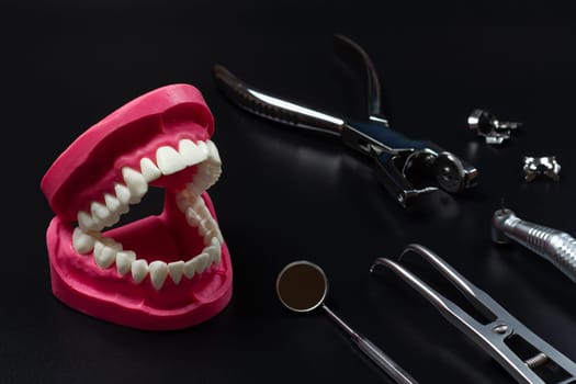 Layout of a human jaw with, the rubber dam forcep, the clamps and the dental hole punch. Head of high-speed dental handpiece with bur and the metal mirror on the black background.