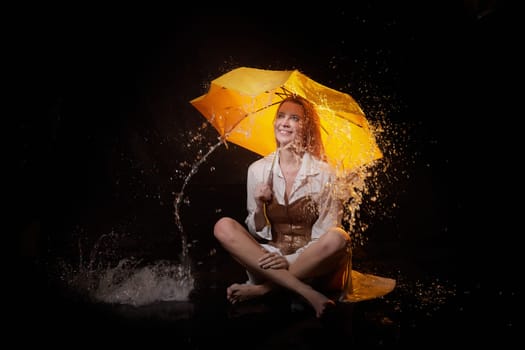 Beautiful sexy skinny girl in a dark hall with splashes of water and yellow umbrella under rain. Female Model blonde woman posing with water on black background in the studio