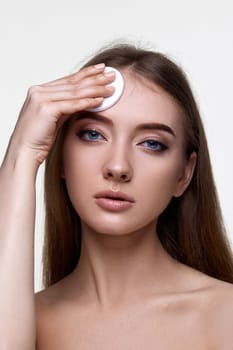 young woman holding white cotton pad for removing makeup isolated on white background