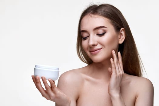 beautiful happy young woman applying skin care cream on her face on white background