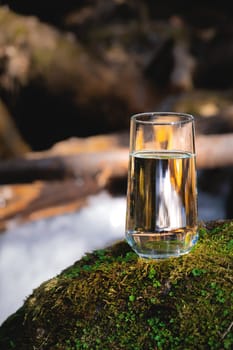 Clean water, healthy concept. Natural drinking water in a glass glass stands on a stone against the backdrop of a river, nature.