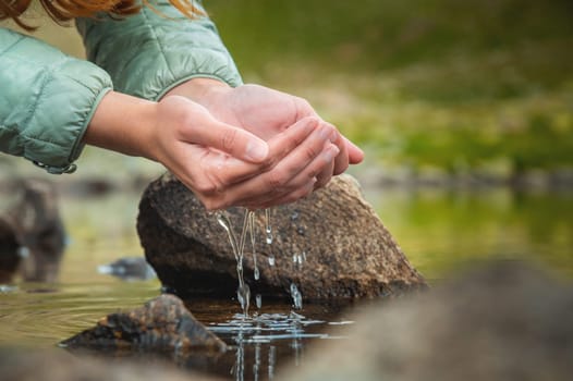 Close-up of a woman's hand pouring water from her palms while trying to drink from a clean water source in nature.