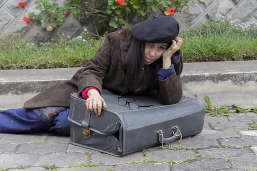 artist lying in the depressed street with her old suitcase and her painter's beret. High quality photo