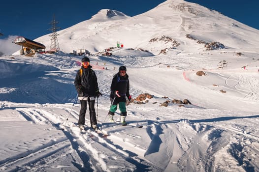 A pair of skiers standing on skis side by side in a helmet and goggles getting ready for the descent. The concept of winter friendly outdoor recreation in the mountains, active recreation, doing winter sport.