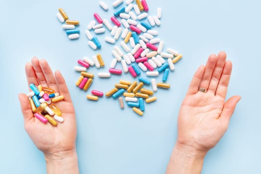 The girl holds a handful of bright vitamins, nutritional supplements and medicines in her palms on a blue background. Concept of medicine and healthcare