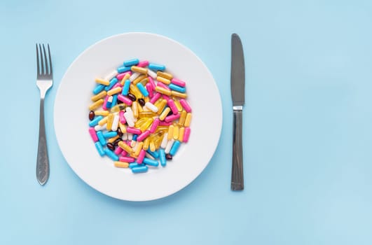 Tablets, capsules, vitamins and natural organic food supplements on a white plate on a blue background. Minimal modern pharmacy or healthcare concept