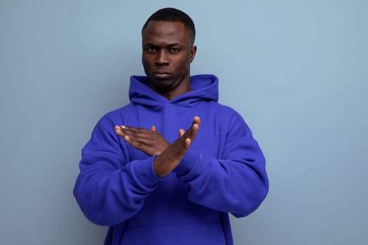 close-up of a serious pensive american young guy in a sweatshirt with a hood with his arms crossed on a studio background with copy space.