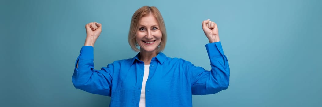 close-up of a joyful middle aged woman in a blue shirt on a blue background with copy space.
