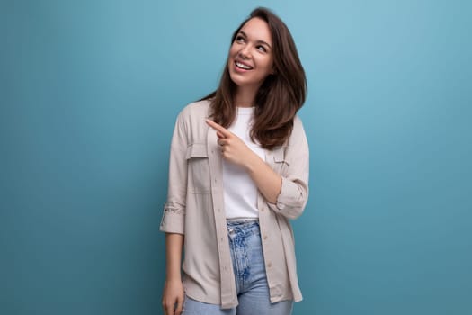 charming brunette 30s woman in shirt and jeans smiling on blue background.