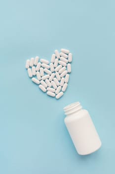 White pills in the shape of a heart came out of a jar on a blue background, health and heart problems together with a plastic jar. The concept of medicine and health care. Place for writing