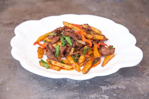 fried french fries and meat with pepper and spices on a white plate.