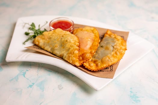 fried delicious chebureks with sauce on a white plate.