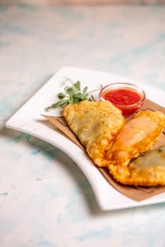 fried delicious chebureks with sauce on a white plate.