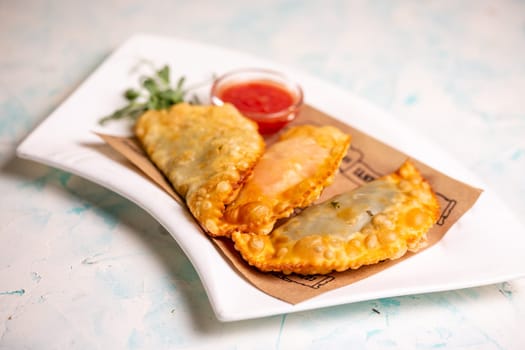 fried delicious chebureks with sauce on a white plate.