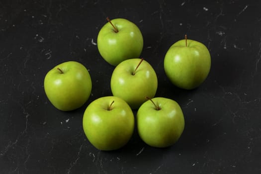 Six green / yellow apples on black marble board.