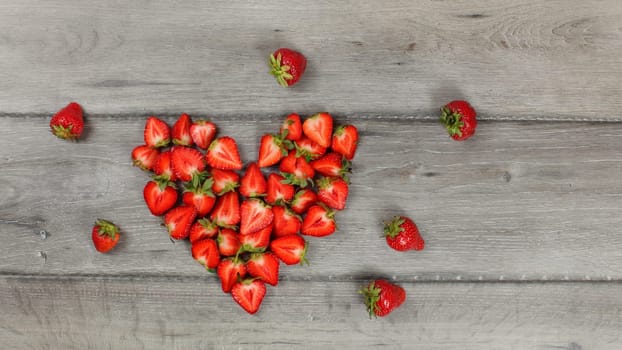 Strawberries cut to halves pieces, arranged in heart shape, on gray wood desk. Top down view.