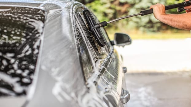 Car washed in self serve carwash on a sunny day. Detail of brush cleaning side window glass covered in shampoo foam