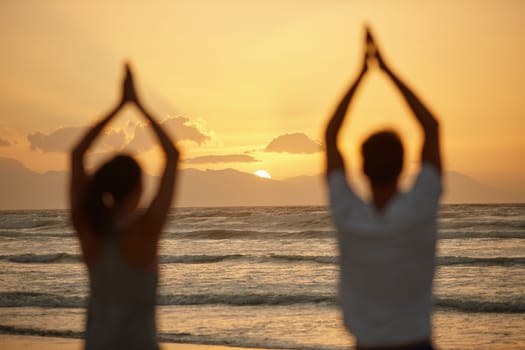 Appreciating the beauty of nature while doing yoga. Rearview shot of a couple doing yoga on the beach at sunset