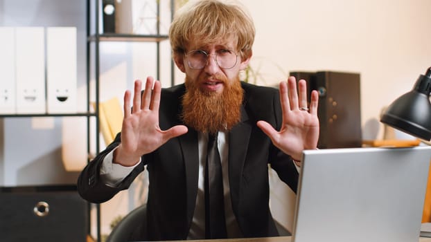 Stop. Young businessman guy working on laptop, warning of finish, prohibited access, declining communication, body language, rejection, danger trouble. Manager man freelancer at home office workplace