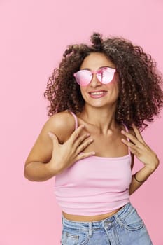 Happy woman afro curls hair dancing on a pink background in summer pink t-shirt jeans and glasses, summer vibe, copy space. High quality photo