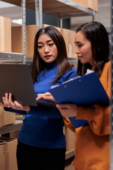 Warehouse managers checking product inventory analysis report data on laptop while managing parcles dispatching operations. Delivery service workers using order fulfillment software in storage room