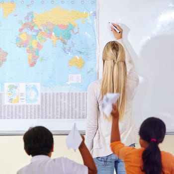 Classroom mischief. A geography teacher writing on the white board as her students throw paper planes