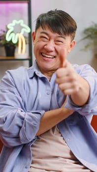 Like. Happy excited asian man looking approvingly at camera showing thumbs up, like sign positive something, good great news, positive feedback. Adult chinese guy at home living room. Vertical shot