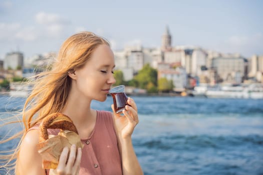 Woman in Istanbul having breakfast with Simit and a glass of Turkish tea. Glass of Turkish tea and bagel Simit against golden horn bay and the Galata Tower in Istanbul, Turkey. Turkiye.