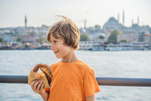 Boy in Istanbul having breakfast with Simit and a glass of Turkish tea. Glass of Turkish tea and bagel Simit against golden horn bay in Istanbul, Turkey. Turkiye. Traveling with kids concept.