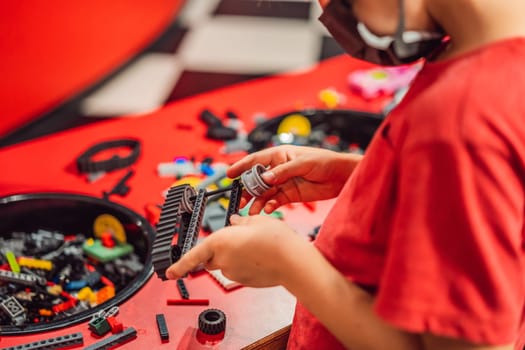 A boy in a medical mask plays with a constructor. child playing and building with colorful plastic bricks table. Early learning and development.