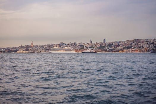 Huge cruise ship docked at terminal of Galataport, located along shore of Bosphorus strait, in Karakoy neighbourhood, with Galata tower in the background.