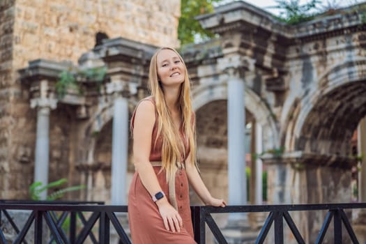 Happy female tourist traveler discover interesting places and popular attractions and walks in the old city of Antalya. Hadrian Kapisi turkey landmark city history. Popular tourist attraction - ancient Roman Hadrian Gate in old town Antalya, Turkey on a summer day. Turkiye.