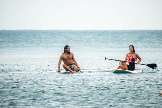 Sea woman and man on sup. Silhouette of happy young woman and man, surfing on SUP board, confident paddling through water surface. Idyllic sunset. Active lifestyle at sea or river