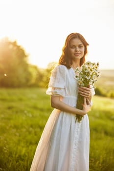 portrait of a woman in a light dress in a field during sunset with a bouquet of daisies in her hands. High quality photo