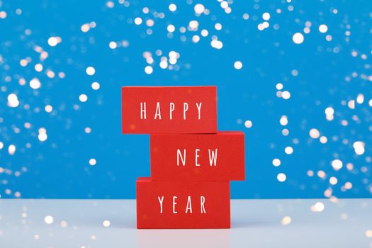 Happy New Year blue minimal trendy concept. Modern composition with red toy blocks with written Happy New Year text against blue background with bokeh