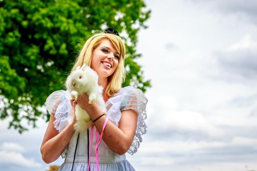 Attractive female model in Alice costume, with white rabbit, in wonderland.