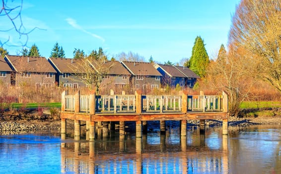 A small wooden deck at the lake shore, with residence buildings in the back ground.