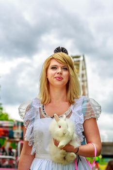 Attractive female model in Alice costume, with white rabbit, in wonderland.