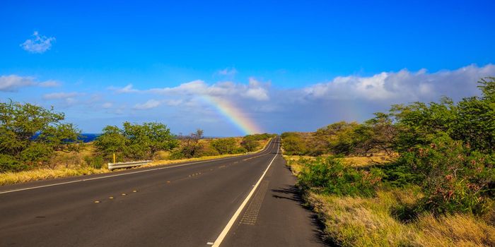 Partial rainbow appears at the end of the highway road, under the sun.