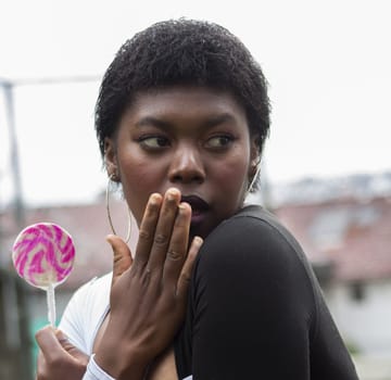 closeup of afro girl with a scared face and a pink lollipop in her hand. High quality photo